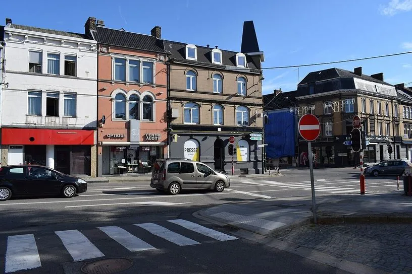 Vue latérale d’un carrefour à Andenne : passages piétons, panneaux STOP au-dessus des feux et panneau rond rouge barré d’un rectangle blanc près du trottoir.