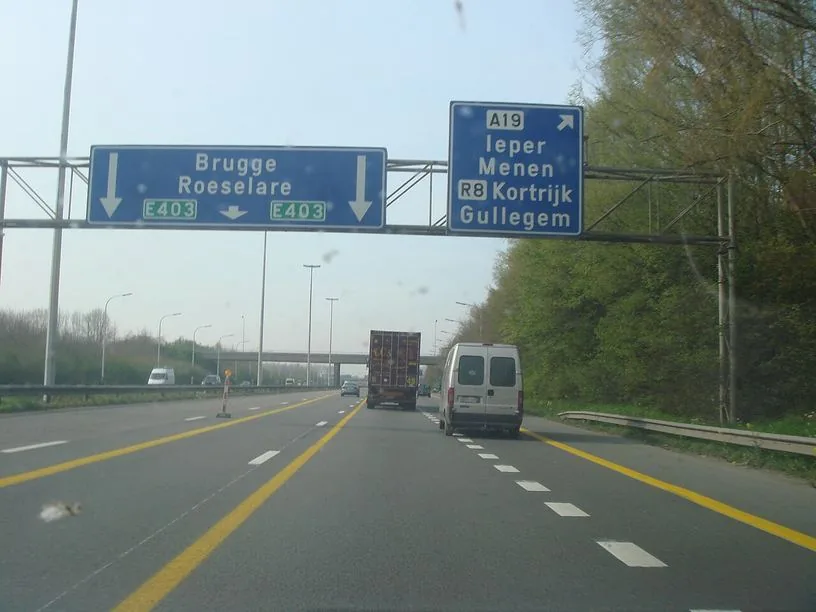Autoroute en travaux avec des marquages orangés décalés par rapport aux lignes blanches ; un camion et des camionnettes circulent devant.
