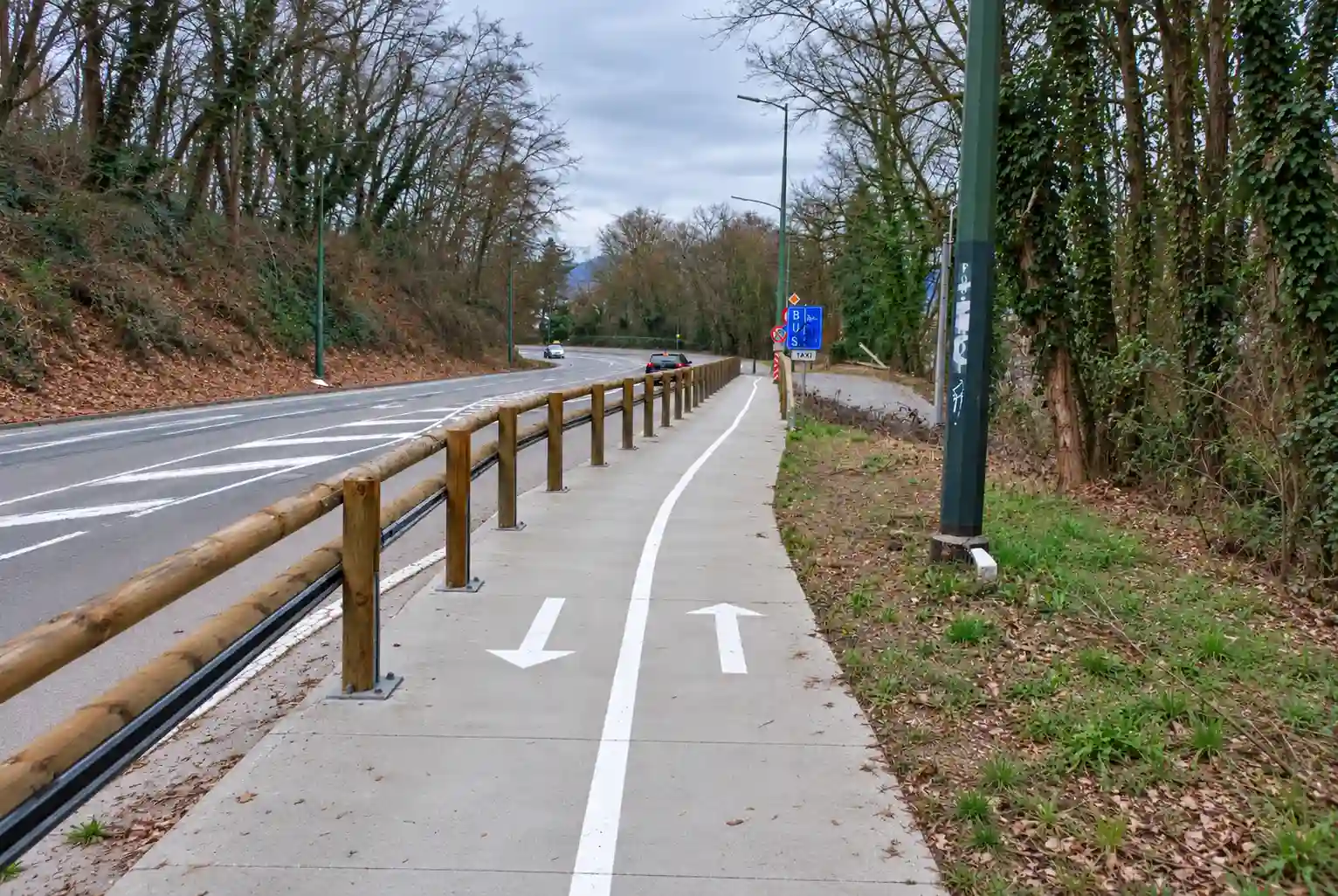 À Angleur, panneau bleu « BUS » avec panneau additionnel « TAXI », près d’un accès latéral ; piste cyclable à deux sens séparée de la chaussée par des poteaux.