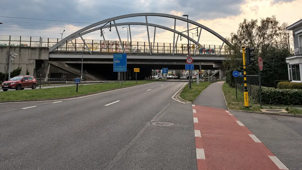 À Anvers, piste cyclable à droite prolongée à travers un accès latéral par deux lignes blanches discontinues sur fond rouge ; signal D7, feu et panneau « 70 » près du pont.