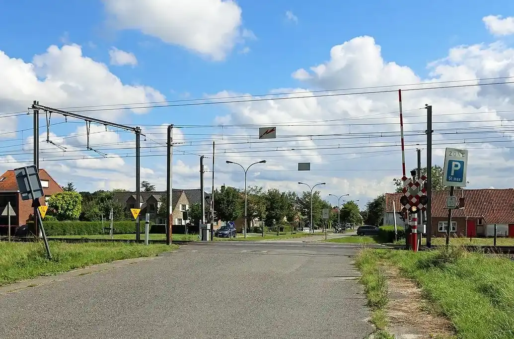 Passage à niveau à Bruges avec barrières levées, feux et croix de Saint-André ; route dégagée au-delà des rails et panneau de stationnement zonal « P 5 t max » à droite.